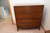 Front-facing shot of a mid-century modern wooden chest dresser showing four closed drawers with curved recessed handles.