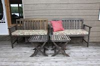 Front view of two teak benches with floral cushions and two matching square side tables on a wooden porch floor, one bench with a pink cushion.