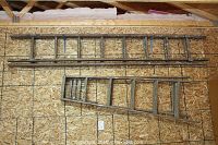 Full view of the two wooden ladders side by side: a long extension ladder and a shorter step ladder on plywood wall background.