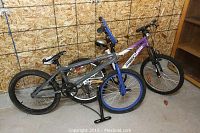 Two bicycles side by side; one white and purple Supercycle and one gray and blue single-speed Shaun White Supply Co bike, with visible tires and frames.