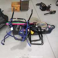 Thule rear mount bike rack laying on floor with blue straps, tennis rackets stacked inside hockey bag and portable stools visible beside it