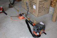Full view of assembled trimmer on concrete floor showing engine, shaft, handles, strap and spool