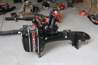 Full side view of Mercury outboard motor on garage floor showing overall length, tiller handle, mounting bracket and general condition
