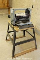 Full view of Delta 12" Portable Planer Model 22-540C mounted on metal stand in a workshop setting, showing the planer body and stand structure.