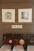 Pair of framed prints on wall above bench, wood wall-mounted Lake Rules sign below prints. On bench are two round wooden plaques and a wooden coat rack with four hooks.