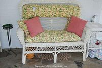 Full front view of white wicker love seat with floral seat and back cushions, and two salmon pink throw pillows.