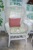 Full view of white wicker chair with pink cushion and floral seat cushion; pink cushion not included in sale.