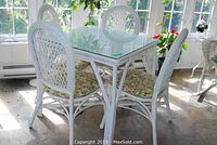 Photo showing the white wicker table with glass top and four matching chairs in a sunroom setting.