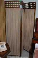 Front and side view of the framed oak folding screen with fabric panels, standing upright in a room next to furniture.