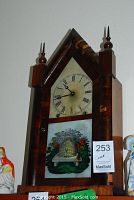 Full view of Victorian steeple clock showing wooden pointed arch case with finials and painted glass panel featuring beehive and flowers.