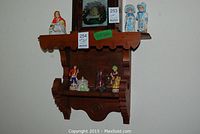 Wooden wall shelf holding various porcelain figurines including Dresden dolls and decorative glass items