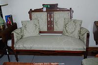Full front view of the restored settee showing mahogany frame and green damask upholstery with two throw pillows