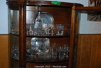 Crystal and silver-plated serving trays displayed inside a wooden cabinet, with several crystal glasses arranged on shelves.