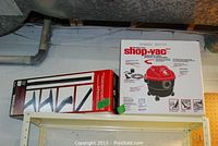 Photo shows the boxed red and black Craftsman Shop Vac and boxed Craftsman vacuum attachments on a shelf.