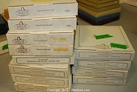 Stacks of Christian Bell Porcelain plate boxes labeled with individual plate titles