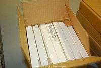 Seven boxed collector plates stored in a cardboard box, with some box tops showing days of the week labels.