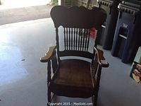 Front view of the antique wooden rocking chair showing the curved armrests, spindle backrest, and contoured seat.