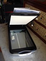 Open Epson scanner showing glass scanning surface and hinged lid on marble countertop.