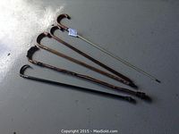 Five wooden canes laid out on floor showing differences in handle style and wear.