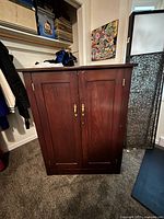 Front view of wood armoire with paneled doors and brass hardware