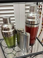 Two colored stainless-steel martini shakers and hip flask
