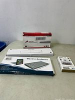 Photo showing all items together: DR Battery notebook battery box, Keychron palm rest, wireless keyboard box, and a small accessory box.