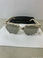 Front view of Gentle Monster sunglasses showing cream-colored frames with black scribble pattern and dark lenses on white background.