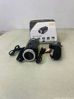 Photo showing the black HD digital video camera with attached adjustable flip-out screen, accompanied by two USB cables, one external microphone, and the original box with HD branding and feature icons visible.