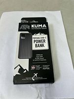 Photo of Kuma Outdoor Gear portable power bank box showing front with product name, capacity, input/output specs, and features.