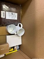 Box contents showing two white ceramic mugs, brown bathtub pillow, and sealed boxes