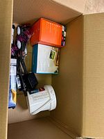 Box containing various miscellaneous items including electronics, household items, and small boxes.