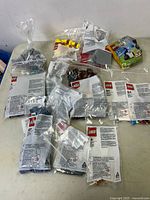 Multiple sealed LEGO sets in original plastic bags spread on a surface, plastic labeling visible on many bags, showing LEGO branding and safety warnings.