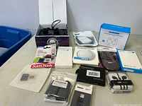 Overview of lot items on table showing controller, memory card packages, cables, chargers, and adapters in boxes