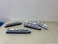 Five model vessels shown side by side on a flat surface: three submarines and two cruise ships.
