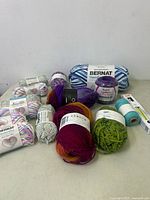Multiple skeins of new Bernat Handicrafter cotton yarn plus other yarns in various colors including purple, green, and orange-red glaze with a small spool of turquoise thread.