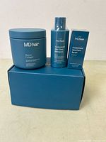 Photo of MDhair Marine Collagen jar, Customized Hair Care Shampoo bottle, and boxed Customized Hair Care Serum on top of blue MDhair box.