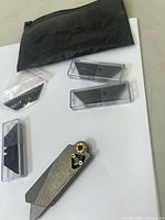 Overview photo of lot showing utility cutter, three replacement blade cases, small bag of screws, and black fabric pouch on white background.