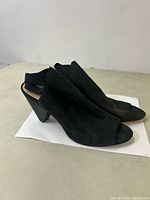 Side view of black suede peep-toe heeled shoes with elastic side panel and block heel.