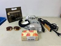 Lot contents on table showing all items together including straightener, skincare starter kit, headbands, sunglasses and soap
