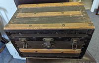 Front view of black wooden mini steamer trunk showing wood straps, rivets, and metal latch with lock.