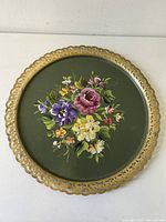 Top view of metal tray showing floral painting with pink, purple, yellow flowers and gold scalloped edge on dark green background.