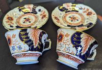 Side profile of the two Royal Crown Derby Battersea tea cups with saucers showing the intricate floral and leaf design with cobalt blue, burnt orange, and gold accent colors.