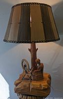 Full view of the carved wood table lamp showing the colonial lady at spinning wheel, wooden base and unique wooden slat lampshade.