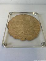 Front angled view of the polished Lucite frame featuring the circular aged newspaper sheet inside, showing edges and surface detail.