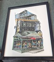 Photo of framed colorful print showing 'The Pilot Tavern' building with architectural details and people inside.