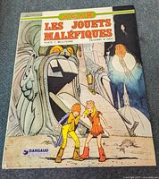 Front cover of the comic book Les Jouets Maléfiques showing two children in colorful outfits in front of a large mechanical or carved face structure, with vibrant sci-fi/fantasy style artwork.