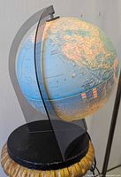 Side view of the vintage illuminated world globe on its black base with clear acrylic semi-circular support.