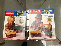 Two unopened boxes of Playskool Lincoln Logs showing front packaging with children playing with the wooden logs, one box 103 pieces, the other 162 pieces.