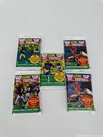 Five unopened 1990 Score NFL Football trading card packs, showing front artwork with NFL players and promotional text.