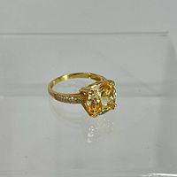 Close-up side angle of the gold plated ring showing the large yellow cushion-cut gemstone and pave set stones on the shoulders of the band.